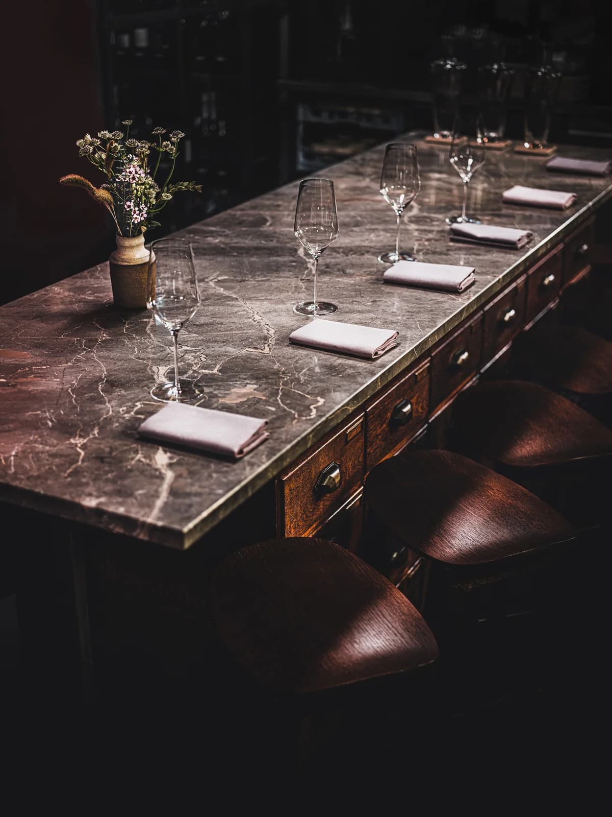 A marble counter set with wine glasses and surrounded by leather stools